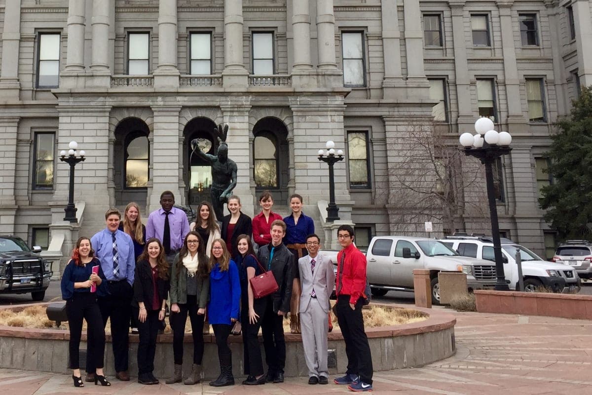 High school students in business dress standing together in front of the gold-domed Colorado State Capitol.