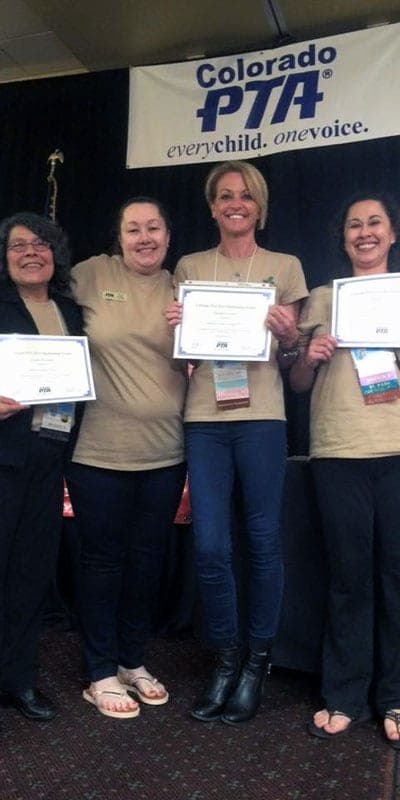 Four Colorado PTA volunteers holding award certificates on stage beneath a Colorado PTA banner.