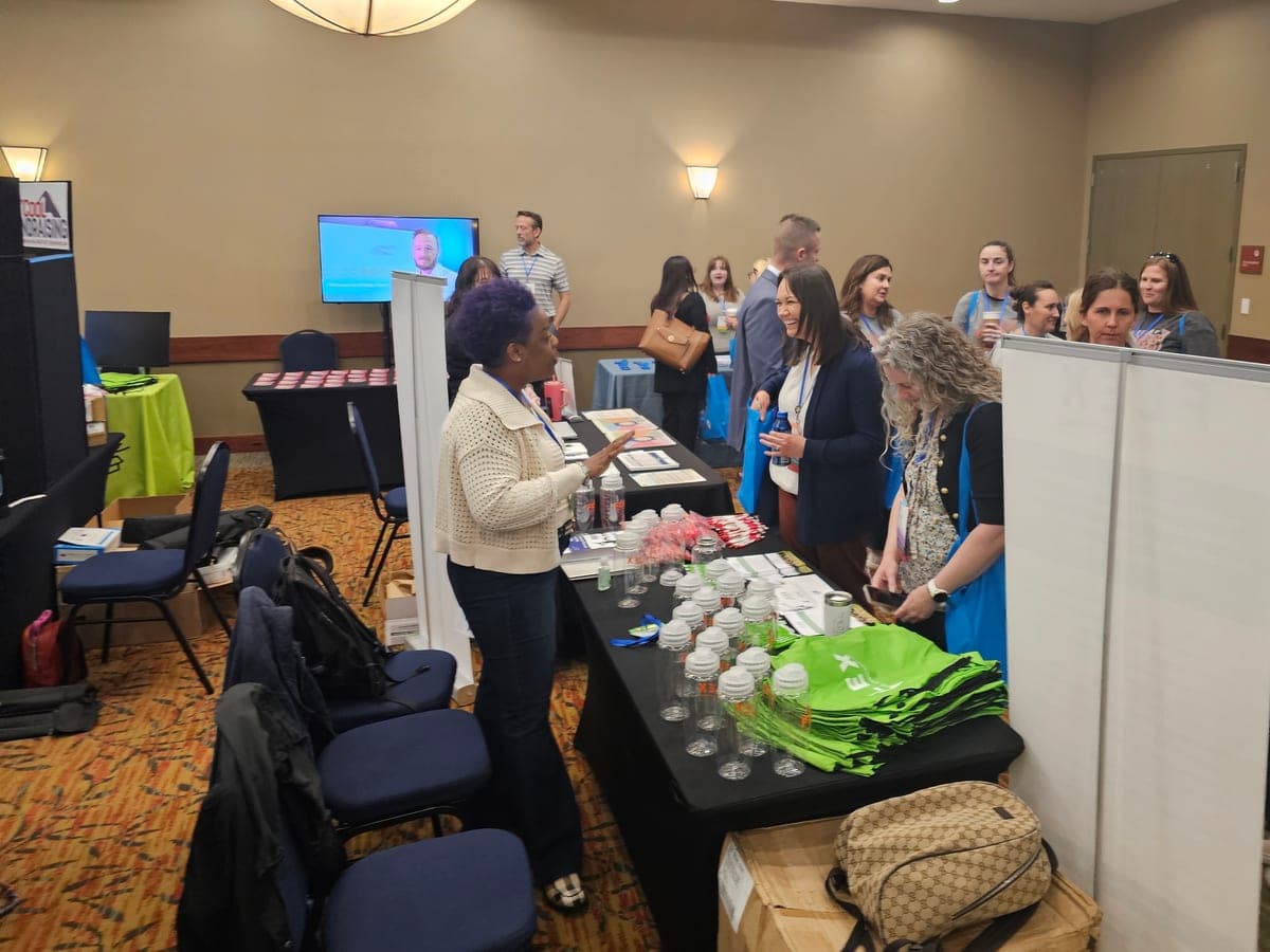 A vendor talks with smiling attendees at an exhibitor table at the 2024 Colorado PTA convention.