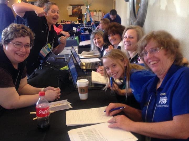 Smiling volunteers in blue Colorado PTA shirts working at a convention registration table.