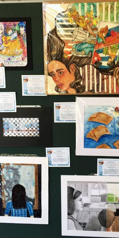 A wall of framed Reflections student artwork with label cards.