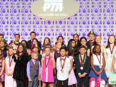 Young award winners wearing medals stand together on stage in front of a National PTA backdrop.